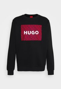 Sudadera negra con cuello redondo; presenta un gráfico rectangular rojo prominente con patrones en espiral y la palabra "HUGO" en blanco.