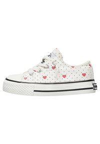 Sneakers in tela bianchi con pois neri e motivi a cuori rosse. Presentano una punta in gomma e una suola in gomma testurizzata con strisce nere.