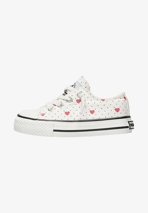 Sneakers in tela bianchi con pois neri e motivi a cuori rosse. Presentano una punta in gomma e una suola in gomma testurizzata con strisce nere.