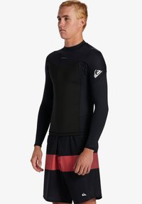 Čierna surf tričko s dlhými rukávmi, hladkou textúrou a priliehavým strihom, v kombinácii s čiernymi šortkami so širokým červeným horizontálnym pruhom.