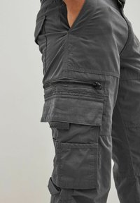 Gray cargo pants made of soft fabric, featuring multiple pockets, visible stitching, a zippered side pocket, and textured accents.