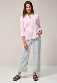 Blouse rose clair à manches longues avec des rayures verticales blanches, design à col en V. Associée à un jean large bleu clair et des sandales navy à enfiler.
