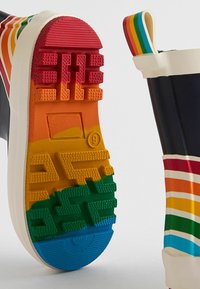 Botte de pluie en caoutchouc avec un corps bleu marine, des accents rayés multicolores et une semelle texturée présentant un dégradé de rouge, orange, jaune, vert et bleu.
