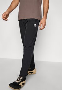 Calças atléticas pretas com corte justo, feitas de tecido leve, com logótipo branco na coxa esquerda e bolsos laterais com fecho de correr.