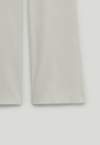 Gros plan sur la partie inférieure d'un pantalon beige clair à jambes droites sur un fond clair.