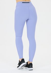 Ljuslila leggings gjorda av stretchigt tyg med hög midja och en liten svart dragkedjeficka på baksidan. Slät textur.