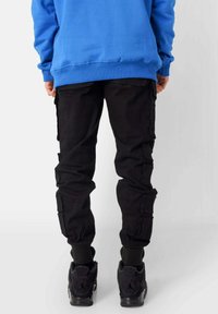 Blauwe sweatshirt en zwarte cargobroek met meerdere zakken en geribbelde boorden. Zwarte sneakers maken de outfit compleet.