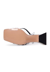 Mustasukat korkokengät, joissa on neliömäinen kärki, läpinäkyvät hihnat ja teksturoitu musta korko. Pehmeä beige pohja, jossa on hienovaraisia uria pitoa varten.
