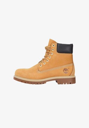 Tan suède laars met een zwarte gewatteerde kraag, metalen oogjes en rubberen zool, voorzien van ton-sur-ton stiksels en een logo aan de zijkant.