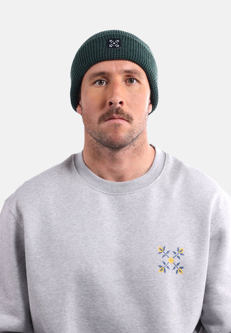 Sweatshirt gris avec un motif floral sur la poitrine gauche ; bonnet vert foncé avec un patch logo ; fond uni.