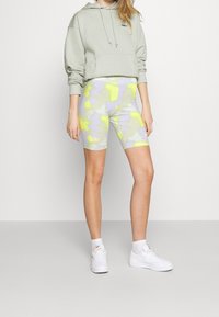 Ljust grå, kort hoodie med logotyp, kombinerad med mönstrade cykelshorts i gult, grönt och lila. Vita sneakers fulländar outfiten.