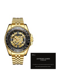 Gouden roestvrijstalen horloge met een zwarte wijzerplaat, Romeinse cijfermarkeringen en een skeletontwerp. Inclusief geïntegreerde gouden armband en merkkaart.