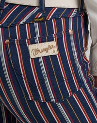 Randiga denim Overall har blå, röd, gul och vita horisontella linjer. En sydd "Wrangler" etikett är synlig på bakfickan.