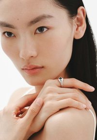 Anillo de plata con un engaste de piedra negra, mostrado en una mano descansando sobre la piel. Diseño suave y elegante; estilo minimalista; sin patrones intrincados.