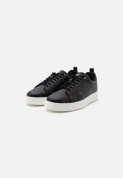 Ζεύγος μαύρα sneakers χαμηλού τύπου με λευκές χοντρές σόλες και μαύρα κορδόνια, εμφανιζόμενα σε απλό ανοιχτό γκρι φόντο.