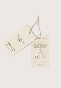 Deux étiquettes de vêtements beiges reliées par une ficelle, l'une portant la mention "Sustainable Cotton COMMITTED,", l'autre détaille la fabrication écologique des vêtements.