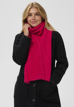 En pink uldhalstørklæde svunget om halsen, kombineret med en struktureret sort frakke. Halstørklædet er livligt og sandsynligvis blødt, med et ensfarvet design.