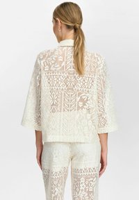 Weiße Spitzenjacke mit lockerer Passform, featuring komplizierte Blumenmuster, 3/4-Ärmel und abgerundetem Saum. Begleitet von passenden Hosen.