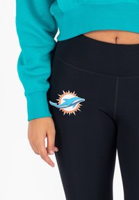 Leggings neri con logo dei Miami Dolphins in blu e arancione, abbinati a un sudore teal con polsini a costine.