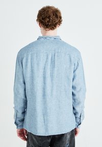 Jasnoniebieska koszula na guziki o luźnym kroju, wykonana z miękkiego materiału. Posiada długie rękawy i detal w postaci karczku z tyłu. Teksturowany, casualowy design.