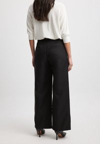 Černé široké kalhoty z hladké látky s jemně strukturovaným pasem a jednou zadní kapsou.