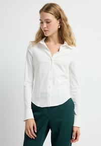 Witte lange mouw knoopsluiting shirt met een zachte textuur en puntige kraag, met een getailleerd silhouet en subtiele verticale strepen.