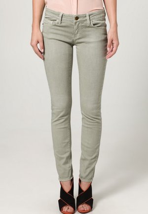 Fitted light green jeans with a smooth texture, five pockets, a metal button, and subtle stitching details, paired with black heeled sandals.