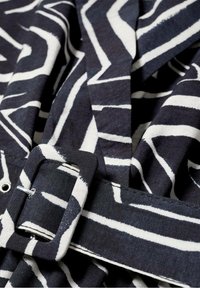 Tela de patrón en blanco y negro con detalle de cinturón; presenta líneas en zigzag atrevidas y una hebilla plana en forma rectangular.