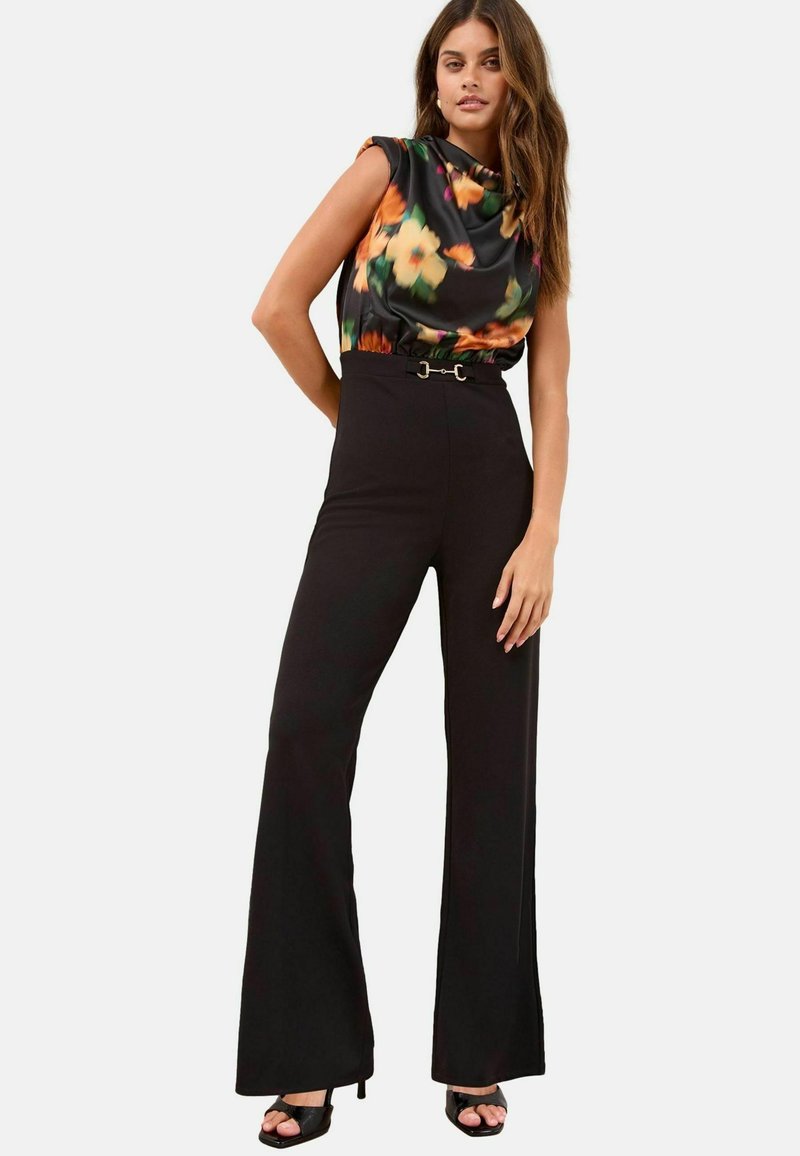 Pantalones negros de talle alto combinados con una blusa de satén con estampado floral y cuello drapeado. Incluye un detalle de cinturón decorativo.