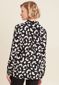 Blusa a maniche lunghe bianca e nera con collo a camicia, dettaglio arricciato sul retro e polsini. Tessuto morbido con forme astratte.