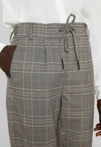 Grå rutiga byxor med dragsko i midjan, sidofickor och en strukturerad yta med ett rutmönster över hela.