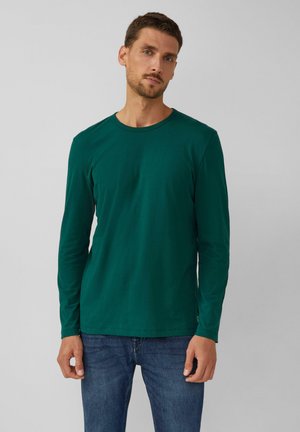 Dunkelgrünes Langarm-T-Shirt aus weichem, glattem Stoff mit Rundhalsausschnitt und ohne sichtbare Muster. Kombiniert mit blauen Jeans.