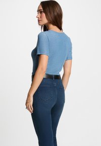 Top azzurro chiaro a maniche corte con una texture luccicante, abbinato a jeans scuri a vita alta con tasche posteriori.
