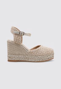 Zapato de cuña de esparto con parte superior de textil beige trenzado, cinta en el tobillo con hebilla plateada y suela gruesa de cuerda tejida con un acento metálico.