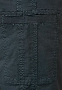 Tissu sombre avec une texture douce, présentant une grande poche arrière et des accents de couture noire visibles le long des coutures.