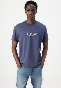 Camiseta de algodón azul marino, de manga corta, con el texto "REPLAY SINCE 1981" impreso en blanco en el pecho. Ajuste clásico.