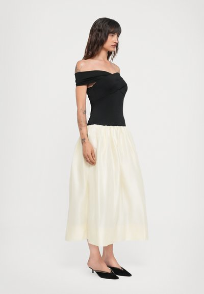 Off-shoulder sort top med en knude detalje, parret med en ankellang elfenbensfarvet nederdel med en samlet talje, båret med sorte hæle.