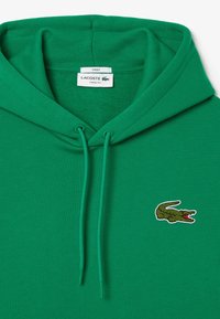 Sudadera de algodón verde con cordón, que presenta un logo de un cocodrilo bordado en verde oscuro y rojo en el área del pecho izquierdo.