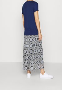 Top blu navy a maniche corte abbinato a una gonna lungo fino alla caviglia con un motivo ornamentale in blu e nero, completato da calzature bianche.