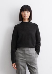Pulover negru din tricot cu guler rotund și mâneci lungi, asociat cu o pereche de pantaloni gri cu carouri, având o croială ajustată și picioare drepte.