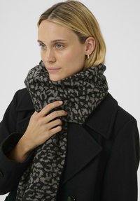 Knitted black and gray leopard print scarf with a soft texture, styled loosely around the neck. Warm and oversized design for comfort.