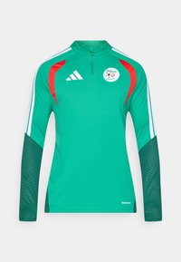 Zöld, hosszú ujjú sportmez, magas gallérral, piros vállbetétekkel, fehér Adidas csíkokkal, és egy kerek logóval, amelyen focilabda látható.