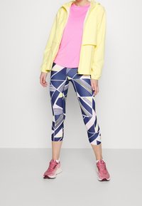 Yellow lightweight jacket, pink T-shirt, geometric patterned navy capris, and pink athletic shoes. Fabric appears breathable and stretchy.