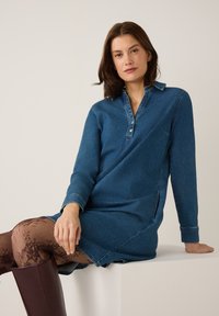 Donkerblauwe denim jurk met lange mouwen, een knoopsluiting bij de kraag en zijslits. Gekocht in combinatie met gestreepte bruine maillots en hoge bruine laarzen.