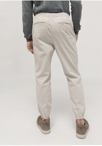 Light beige jogger pants with elastic cuffs, two back pockets, and a relaxed fit, made from soft fabric. Worn with gray sneakers.