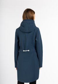 Giacca impermeabile blu navy con cappuccio, vita regolabile con cordino e texture liscia. Presenta un design semplice e dettagli minimalisti.