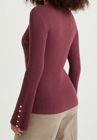 Ribbed burgundy sweater with long sleeves; features golden button accents at the cuff; smooth texture, fitted design, and lightweight material.