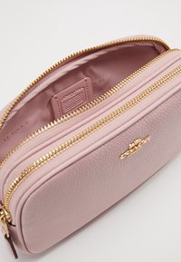 Vaaleanpunainen nahkainen kosmetiikkalaukku, jossa on kultaiset yksityiskohdat ja tekstuuripinta. Varustettu vetoketjulla ja sisäisellä nimilapulla.