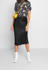 Haut à manches courtes noir à motif floral, jupe midi en satin noir, et bottines blanches. Sac bandoulière jaune qui apporte du contraste.