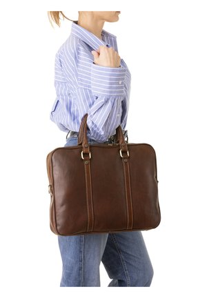 Persoon in een blauw gestreept shirt en spijkerbroek die een bruine leren aktetas bij de handvatten over zijn schouder draagt.